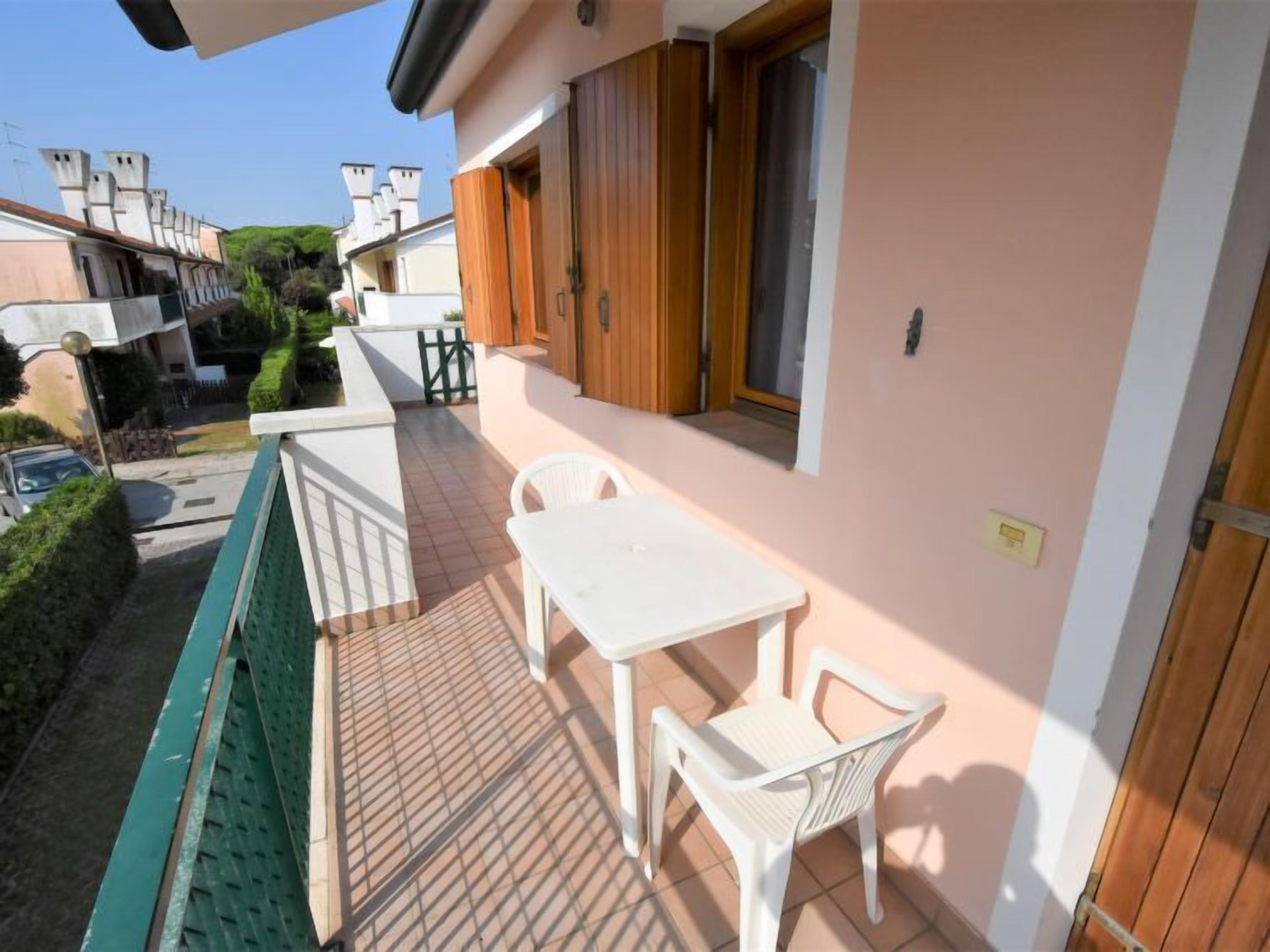 Un balcon avec une table blanche et deux chaises, une porte en bois et une fenêtre avec des volets en bois.