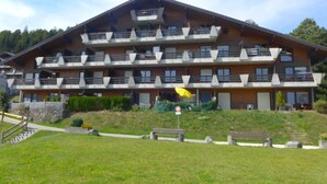 Un hotel de varios pisos con balcones, una escalera que conduce a la entrada y un espacio con césped al frente.