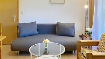 Ein Wohnzimmer mit einem grauen Sofa, einem Glastisch und einer kleinen weißen Vase mit Blumen.