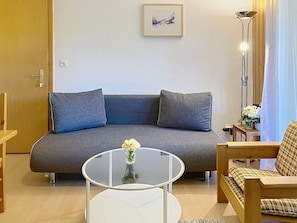 A living room with a grey sofa, a glass coffee table, and a small white vase with flowers.