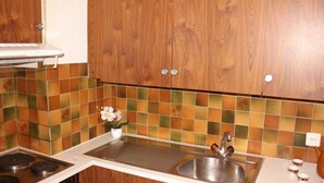 Una cocina con gabinetes de madera, salpicadero azulejado, un lavamanos de acero inoxidable y una estufa.