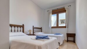Une chambre d’hôtel avec deux lits simples, une petite table de chevet avec une lampe, une fenêtre avec des rideaux et une table de nuit en bois.