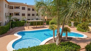 Une piscine entourée de palmiers et un immeuble à plusieurs étages doté de balcons.