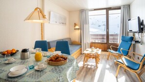 Une chambre d’hôtel confortable avec un coin repas, un canapé, une télévision et une fenêtre donnant sur un paysage enneigé.