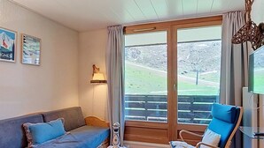 Une pièce comprenant un canapé, deux fauteuils, une table, une lampe, un téléviseur et une grande fenêtre donnant sur un paysage.
