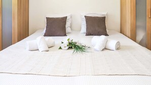 A neatly made bed with white linens and two brown pillows, a small bouquet of white flowers, and towels on the bed. - Rosablanche D35 by Interhome (Siviez-Nendaz)