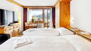 Habitación de hotel con cama, escritorio, televisor y vistas a un paisaje montañoso.