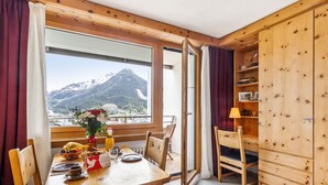 Una mesa de madera con sillas, un florero con flores y vista a la montaña.