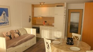 Un espace de vie compact comprenant un coin cuisine, une table à manger pour deux personnes et un canapé agrémenté de coussins décoratifs.