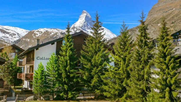 Un chalet de montagne avec une enseigne portant le nom « Collon », situé devant des sommets enneigés.