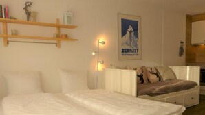 Une chambre d’hôtel avec deux lits, une étagère en bois avec des livres et une tête de cerf, une affiche au mur et une lampe de chevet.