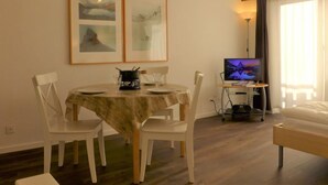 Un coin repas avec une table dressée pour deux personnes, un téléviseur posé sur un meuble et des œuvres d’art encadrées accrochées au mur.