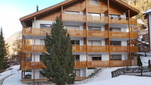 Un hôtel à plusieurs étages doté de balcons en bois, avec une piste de ski en arrière-plan et un sol recouvert de neige.