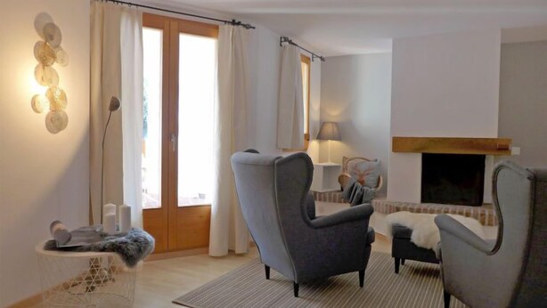 Un salon avec une cheminée, deux fauteuils, un canapé, une table basse ronde et une petite table d’appoint sur laquelle se trouve un chat.