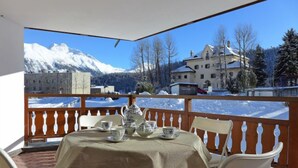 Un balcon avec une table préparée pour le thé, d’où l’on peut admirer un paysage montagneux enneigé et des bâtiments.