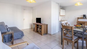 Ein gemütlicher Wohnbereich mit Sofa, Fernseher auf Holzgestell, Esstisch mit Stühlen sowie Küchenzeile mit Schränken und Spüle.