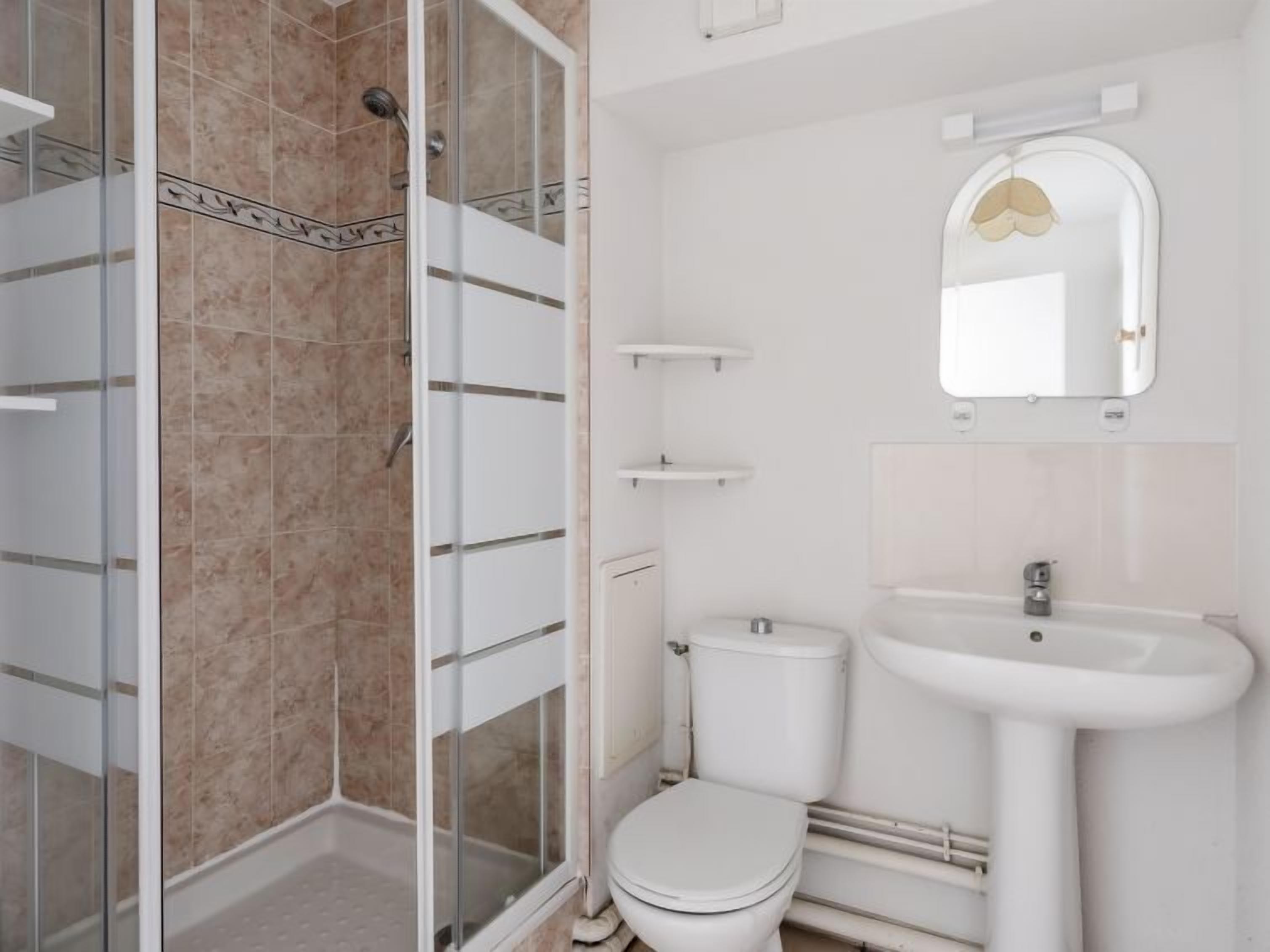Ein Badezimmer mit Duschkabine aus Glas, Toilette und Waschbecken mit Spiegel darüber.