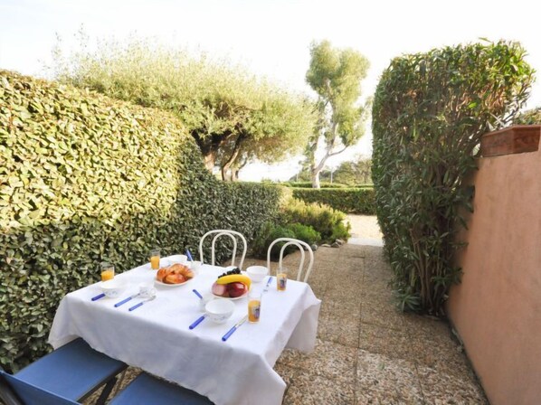 Uma área de refeições ao ar livre com uma mesa posta para dois, cercada por vegetação exuberante e um caminho de pedra.