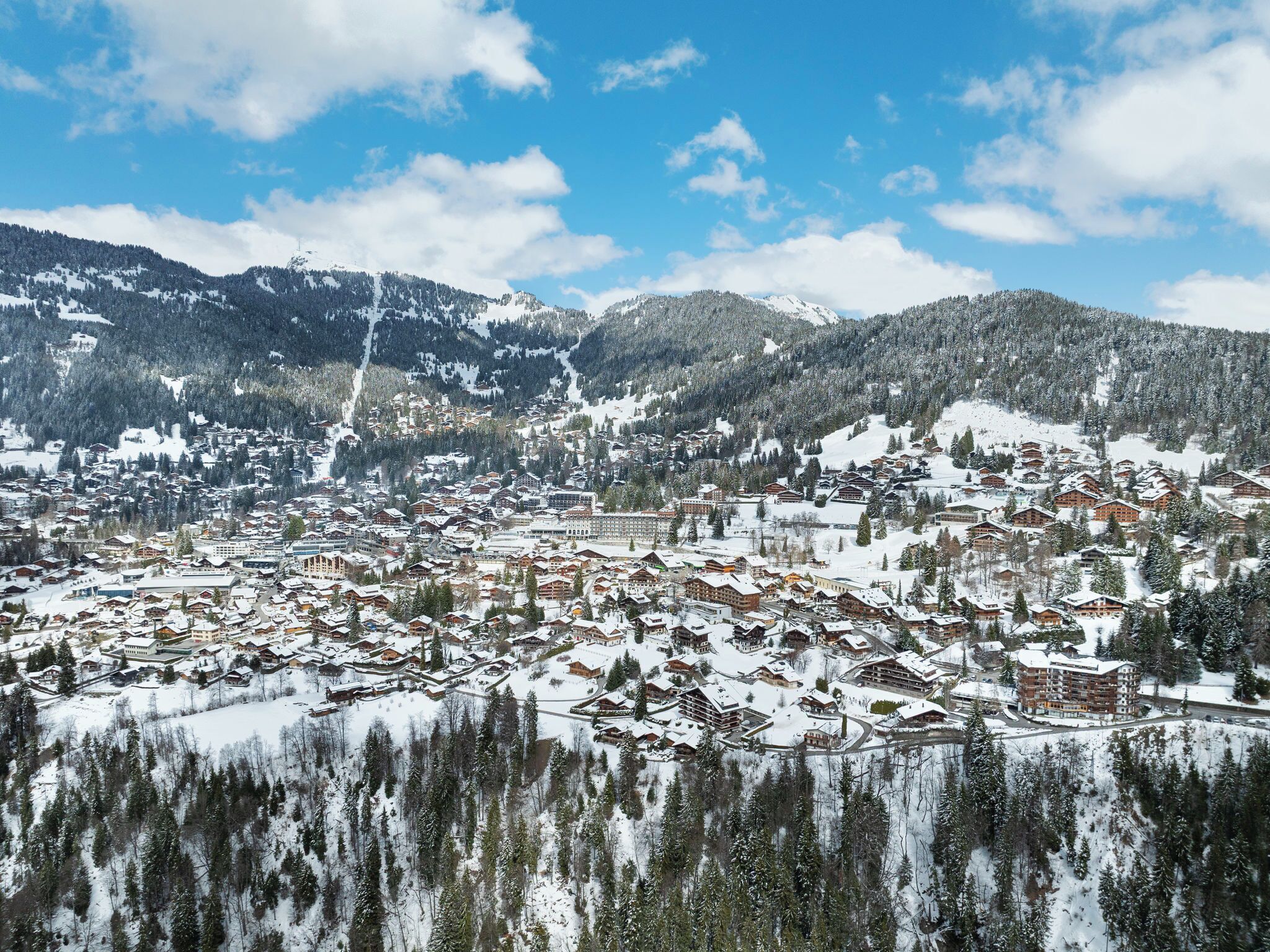 Un pueblo cubierto de nieve en la montaña, con una combinación de edificios tradicionales y modernos, una pista de esquí y amplias zonas boscosas.