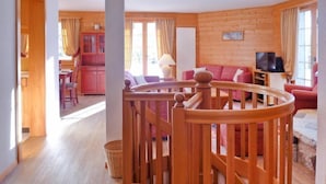 Un interno in legno con una scala, una sala da pranzo e un soggiorno con televisore.