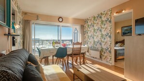 Ein gemütliches Zimmer mit Bett, Esstisch mit Stühlen, Fernseher und Blick auf die Stadt.