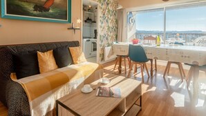 Ein gemütliches Wohnzimmer mit einer Couch, einem Esstisch und Meerblick durch große Fenster.