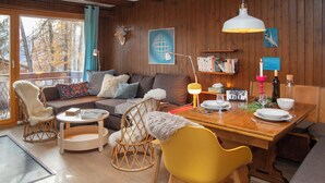 Ein gemütliches Blockhaus-Interieur mit Holzausstattung, einem Esstisch, Stühlen, einer Couch und einem großen Fenster mit Blick auf Bäume.