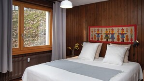 Ein Schlafzimmer mit einem großen Bett, Holzwänden, einem Fenster mit Vorhängen, einem Heizkörper und einem farbenfrohen Wandteppich.