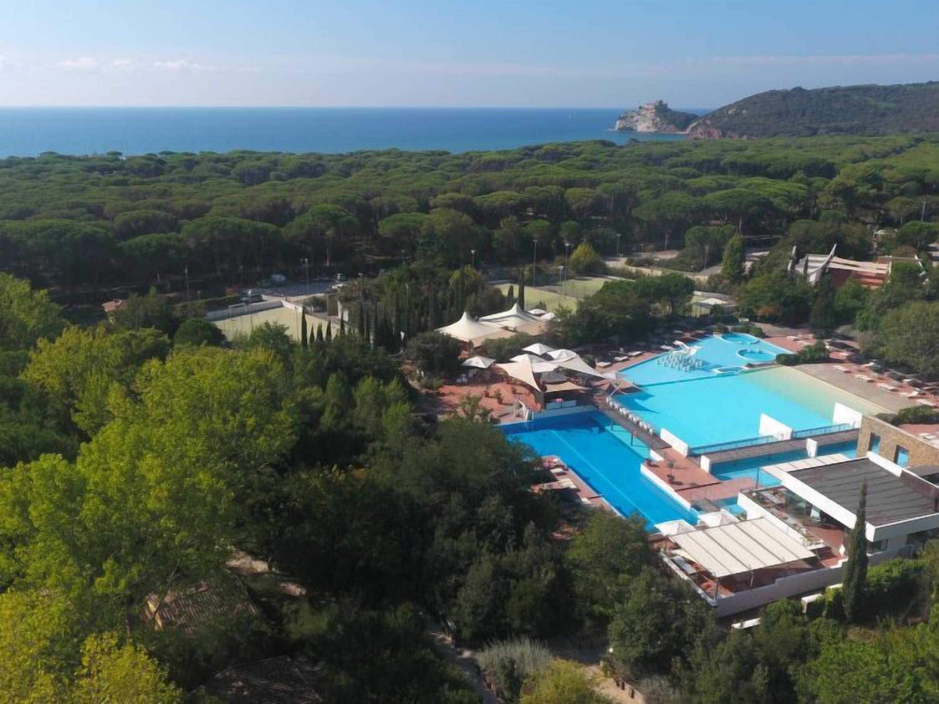 A resort with multiple swimming pools, lush greenery, and a view of the sea.