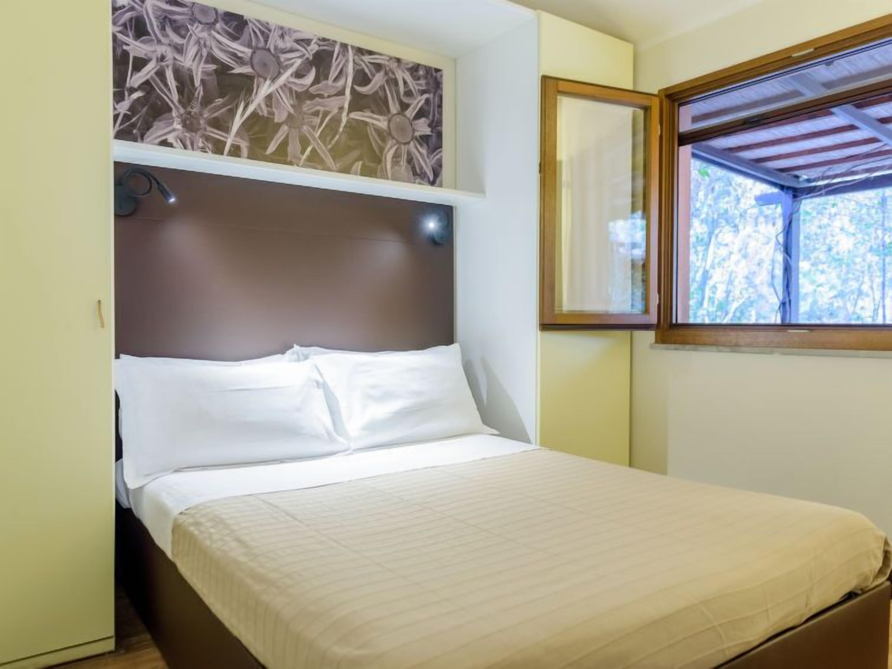A bedroom with a bed, a headboard, a window, and a wall-mounted mirror.