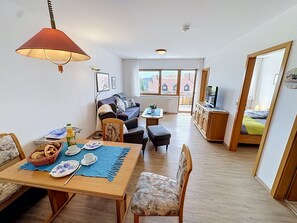 Una sala amueblada con un sofá, una mesa de comedor para dos personas y un televisor sobre un mueble.