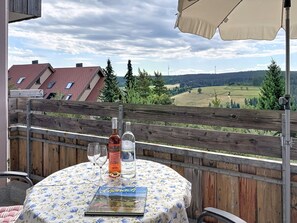A table with a bottle and glasses, a book, and a view of a rural landscape with houses and trees. - Schwarzwaldblick by Interhome (Schonach)