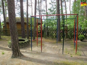 Un parque infantil con columpios y neumáticos colgantes, rodeado de árboles y una valla de madera.