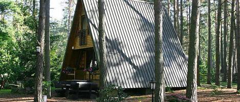 Eine Blockhütte mit geneigtem Dach, umgeben von einem Wald.