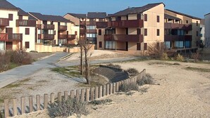 Une rangée d’immeubles résidentiels modernes à plusieurs étages, dotés de balcons, avec une zone de sol sablonneux et une clôture en bois.