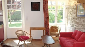 Un salon chaleureux avec un canapé rouge, des fauteuils en osier, une petite table et un lit.