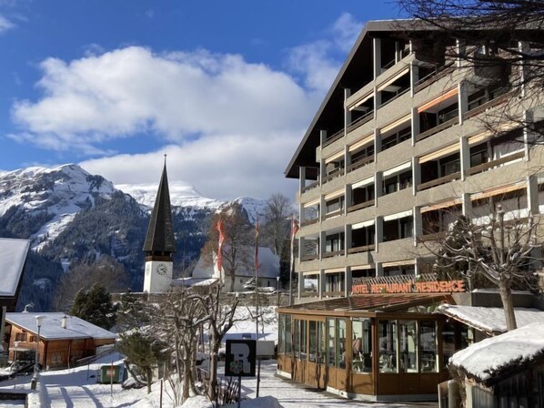 A hotel with a view of snow-capped mountains and a church spire.