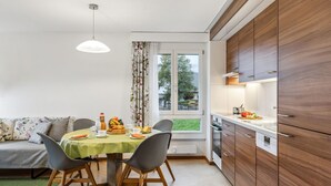 Uma cozinha moderna com armários de madeira, uma mesa de jantar com cadeiras e vista para o exterior através de uma janela.