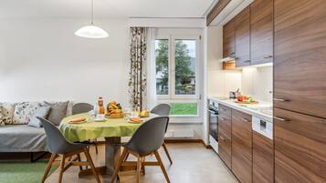 Une cuisine moderne avec des meubles en bois, une table à manger avec des chaises et une vue sur l’extérieur par une fenêtre.