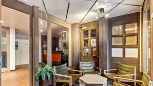 Um interior moderno com paredes de madeira, uma área de estar com cadeiras e uma pequena mesa, e uma porta visível que dá para outro quarto.