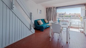 Une pièce avec un escalier, un canapé de couleur turquoise, une table à manger avec des chaises et une vue sur l’eau.