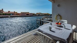 Un balcon avec une table dressée pour deux personnes, d’où l’on peut admirer un plan d’eau avec des bateaux et des bâtiments en arrière-plan.