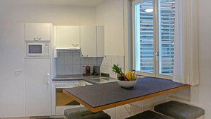 A compact kitchen with white cabinets, a microwave, a stove, and a window with blinds. - Haus Lauber Apt.1 by Interhome (Wengen)