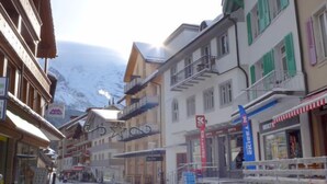 A snow-covered street with buildings, including a hotel with balconies and a sign for a ski resort. - Haus Lauber Apt.1 by Interhome (Wengen)