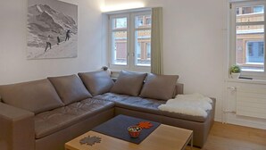 A modern living room with a sectional sofa, a coffee table with a decorative item, and a window with a view of buildings. - Haus Lauber Apt.1 by Interhome (Wengen)