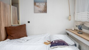 Un dormitorio con cama, espejo, ventana con cortinas, un cuadro en la pared y mesita de noche con lámpara.