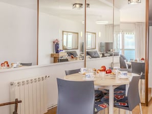 Een eetgedeelte met een ronde tafel, stoelen en een spiegel die de kamer weerspiegelt.