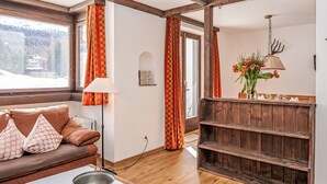 A cozy living room with a wooden bench, a sofa with patterned cushions, a lamp, and a vase with flowers. - Chesa Linaria by Interhome (Silvaplana-Surlej)