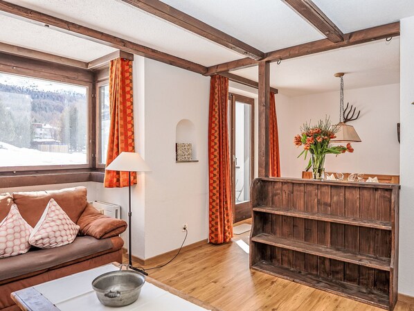 Una sala de estar acogedora con un banco de madera, un sofá con cojines estampados, una lámpara y un jarrón con flores.