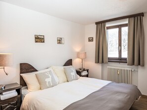 Un dormitorio ordenado con cama, lámparas de noche, una ventana con cortinas y obras de arte colgadas en la pared.